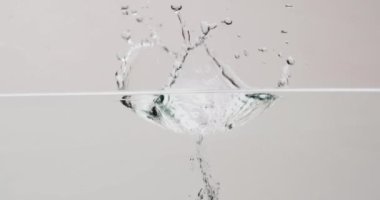 Güzellik ürünü şişesinin suya düşüşünün videosu ve beyaz arka planda fotokopi alanı. Sağlık ve güzellik, makyaj, güzellik ürünleri, renk ve hareket kavramı.