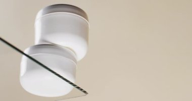 Cam rafta duran güzellik ürünleri küvetlerinin dikey videosu ve beyaz arka planda fotokopi alanı. Sağlık ve güzellik, makyaj, güzellik ürünleri, renk ve hareket kavramı.