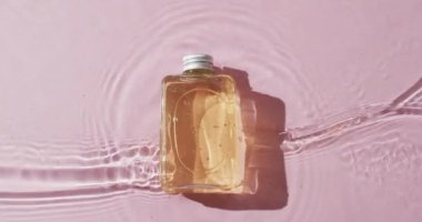 Pembe arka planda fotokopi alanı olan suyun içindeki güzellik ürünü şişesinin videosu. Sağlık ve güzellik, makyaj, güzellik ürünleri, renk ve hareket kavramı.
