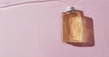 Pembe arka planda fotokopi alanı olan suyun içindeki güzellik ürünü şişesinin videosu. Sağlık ve güzellik, makyaj, güzellik ürünleri, renk ve hareket kavramı.
