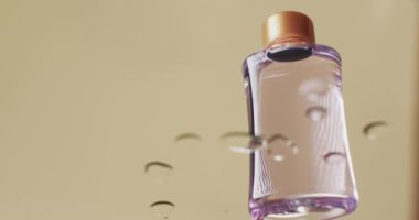 Sarı zemin üzerinde fotokopi alanı olan su içindeki güzellik ürünü şişesinin videosu. Sağlık ve güzellik, makyaj, güzellik ürünleri, renk ve hareket kavramı.