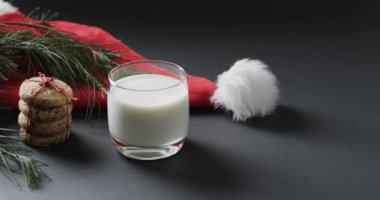 Noel kurabiyelerinin videosu, bir bardak süt, Noel Baba şapkası ve siyah arka planda fotokopi alanı. Noel, pişirme, dekorasyon, gelenek ve kutlama konsepti.