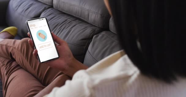 オンラインショッピング スローモーションのためのスマートフォンを使用してソファー上のBiracial女性 小売業 コミュニケーションおよびデジタル インターフェイスによってデジタル生成されるビデオ — ストック動画