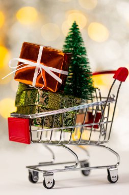 Hediyeli alışveriş arabasının dikey görüntüsü ve fotokopi arkaplanlı noel perisi ışıkları. Noel, dekorasyon, gelenek ve kutlama konsepti.