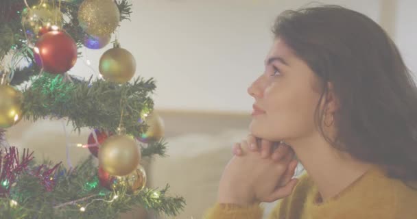 飾られたクリスマスツリーを見ている白人女性の上のメリークリスマステキストバナーのアニメーション クリスマスのお祭りとお祝いのコンセプト — ストック動画