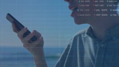 Deniz kenarında akıllı telefondan konuşan Asyalı adama karşı borsa veri işleme animasyonu. Küresel ekonomi ve iş veri teknolojisi kavramı