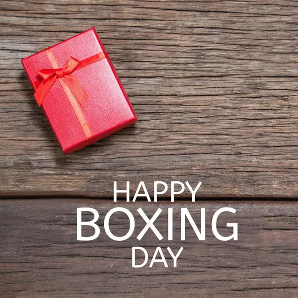 Composite of happy boxing day text over red gift box on wooden table. Shopping, sale, surprise, discount, marketing, template, design, retail, advertise concept.