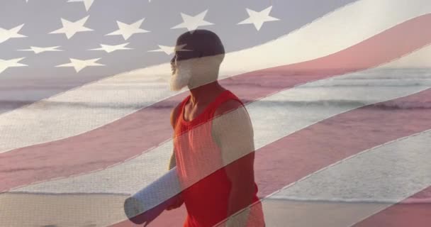 ビーチでヨガマットを持つ上級アフリカ系アメリカ人男性の上にアメリカの国旗のアニメーション アメリカの愛国心 多様性の概念がデジタル生成されたビデオ — ストック動画