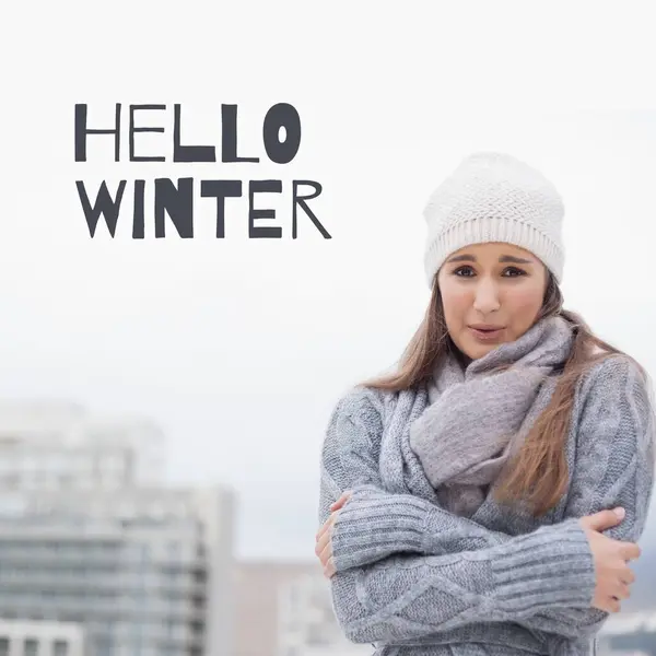 Hello winter text over cold caucasian woman in winter clothes outdoors at christmas time. Celebration of winter, nature, weather, greeting and christmas season, digitally generated image.