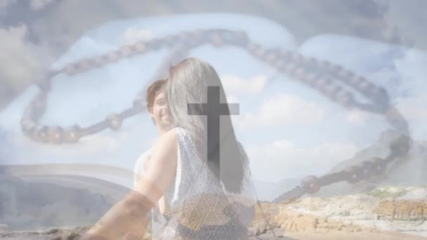 山で十字架のアニメーション ビーチで踊る慎重なカップルの上で聖書のロザリオ デジタル複合 複数の露出 十字架 トータルネスコンセプト — ストック動画