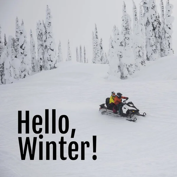 Composite of hello winter text over caucasian couple in snow scooter in winter scenery. Winter, christmas, seasons and celebration concept digitally generated image.