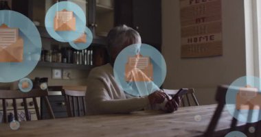 Zarf simgelerinin evde akıllı telefondan kayan yaşlı çift ırklı kadın üzerinde daireler çizmesi. Dijital bileşik, çoklu pozlama, mesaj, şekil, emeklilik ve teknoloji kavramı.