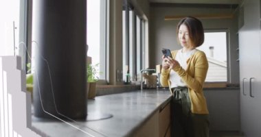 Evdeki mutfakta akıllı telefon kullanan Asyalı kadın hakkında istatistiksel veri işleme animasyonu. Bilgisayar arayüzü ve iş teknolojisi kavramı