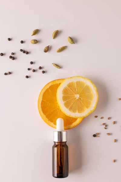 Vertical image of bottle with pipette and oranges and seeds with copy space on white background. Health and beauty, beauty product, make up and colour concept.