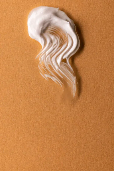 Vertical image of beauty product white cream smudge with copy space on brown background. Health and beauty, beauty product, make up and colour concept.