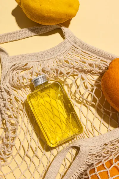Close up of beauty product bottles, oranges and net bag with copy space on yellow background. Health and beauty, beauty product, make up and colour concept.