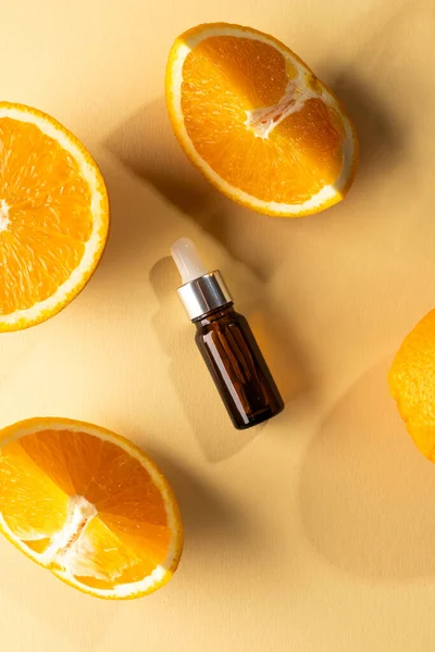 Vertical image of bottle with pipette and oranges with copy space on yellow background. Health and beauty, beauty product, make up and colour concept.