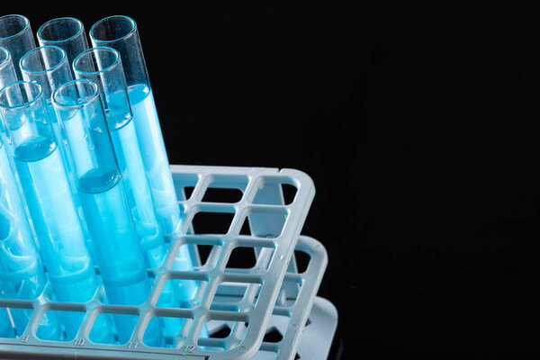 Close up of laboratory test tubes with blue liquid and copy space on black background. Laboratory, science, research and chemistry concept.