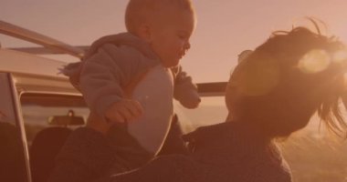 Caddede arabanın yanında bebeği tutan mutlu beyaz bir kadın. Annelik, aşk ve seyahat konsepti