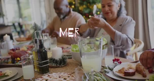自宅でクリスマスディナーで多様なシニアフレンドにメリークリスマステキストのアニメーション カイストマス お祝い 伝統的なコンセプトデジタル生成ビデオ — ストック動画