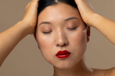 Bej arka planda kırmızı ruj ve oje süren Asyalı bir kadın. Kozmetik, makyaj, kadın modası ve güzelliği, değiştirilmemiş.