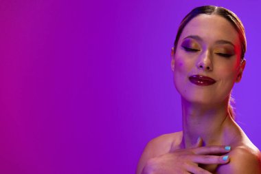 Beyaz kadın mor arka planda kırmızı ruj ve mavi tırnak cilası kullanıyor. Kozmetik, makyaj, kadın modası ve güzelliği, değiştirilmemiş.