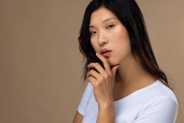 Bej arka planda doğal makyaj ve beyaz tişört giyen Asyalı kadın portresi, fotokopi alanı. Kozmetik, makyaj, kadın modası ve güzelliği, değiştirilmemiş.