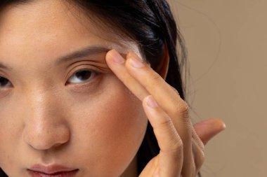 Bej arka planda doğal makyaj yapan Asyalı kadın portresi. Kozmetik, makyaj, kadın modası ve güzelliği, değiştirilmemiş.