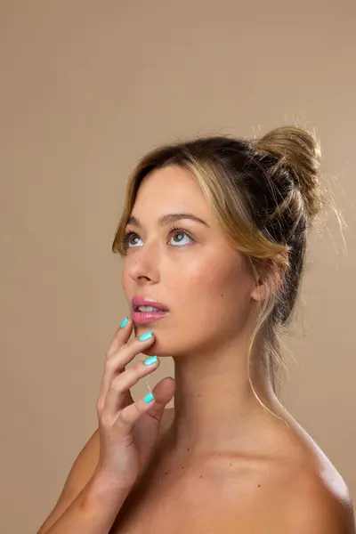 Caucasian woman wearing natural makeup and blue nail polish on beige background, copy space. Cosmetics, makeup, female fashion and beauty, unaltered.