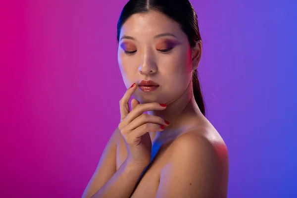 Asian woman with black hair wearing purple eye shadow and red nail polish on purple background. Cosmetics, makeup, female fashion and beauty, unaltered.