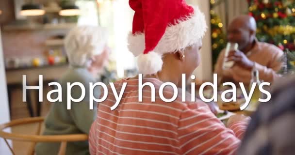 クリスマスのテーブルに座っている多様なシニアの友人に対する幸せな休日のテキストのアニメーション クリスマス お祝いのコンセプトデジタル生成ビデオ — ストック動画