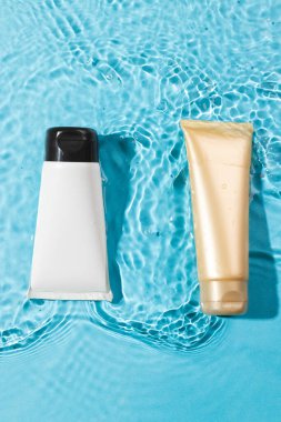 Sudaki güzellik ürünleri tüplerinin dikey görüntüsü ve mavi arka planda fotokopi alanı. Sağlık ve güzellik, makyaj ve güzellik konsepti.