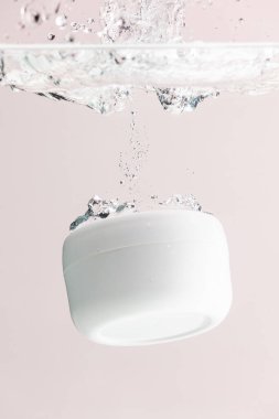 Güzellik ürünleri küvetinin suya düşüşünün dikey görüntüsü, pembe arka plandaki boşluğu kopyalamak. Sağlık ve güzellik, makyaj ve güzellik konsepti.