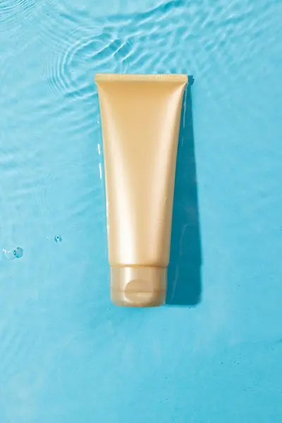 Vertical image of beauty product tube in water with copy space background on blue background. Health and beauty, make up and beauty concept.