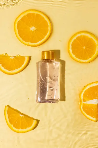 Vertical image of bottle and orange slices in water, copy space on orange background. Health and beauty, make up and beauty concept.