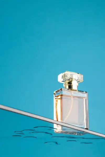 Vertical image of beauty product perfume bottle on glass shelf, copy space on blue background. Health and beauty, make up and beauty concept.