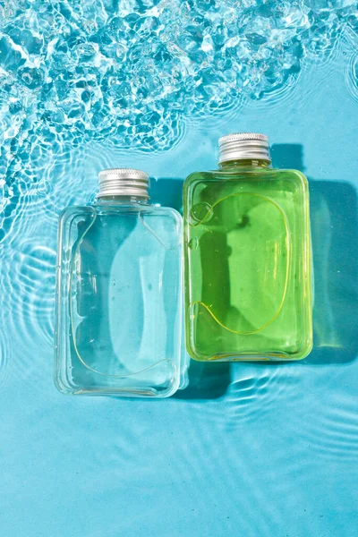 Vertical image of beauty product bottles in water with copy space background on blue background. Health and beauty, make up and beauty concept.