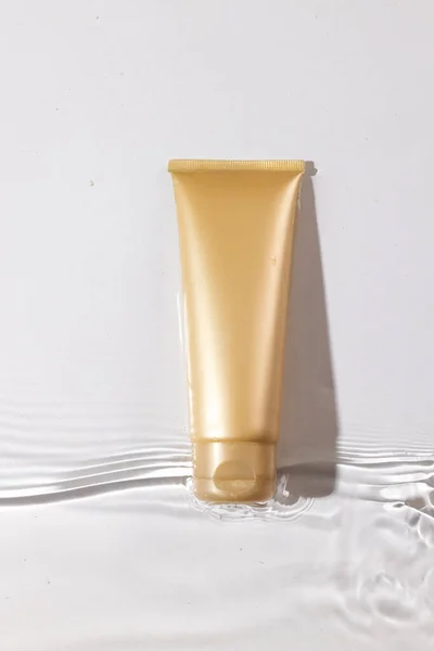 Vertical image of beauty product tube in water with copy space on white background. Health and beauty, make up and beauty concept.
