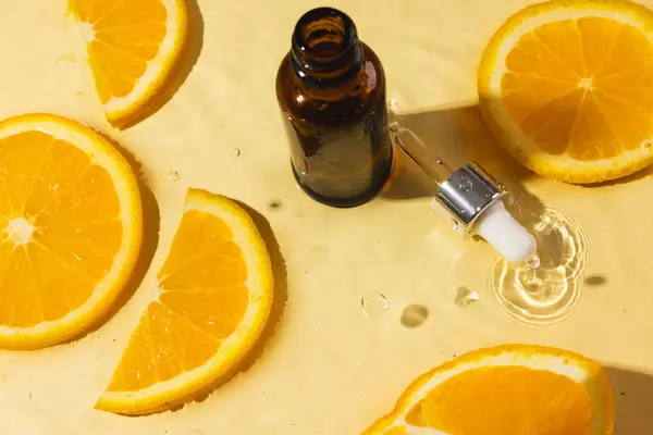 Beauty product bottle with pipette and orange slices in water, copy space on orange background. Health and beauty, make up and beauty concept.