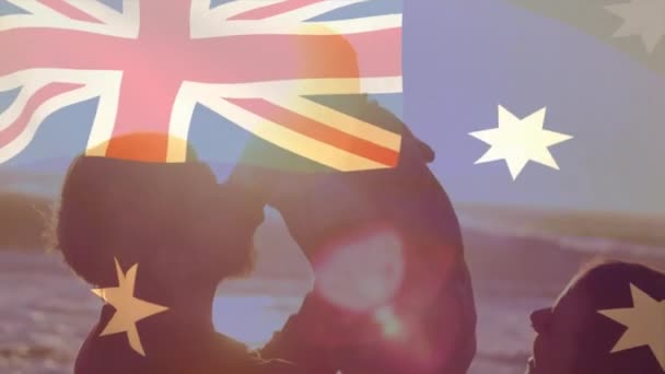 在阳光灿烂的海滩上抱着孩子的快乐的高加索父母身上升起了澳大利亚国旗 Australia Summer Family Parenthood Childhood Vacation Ations Travel Patriotism — 图库视频影像