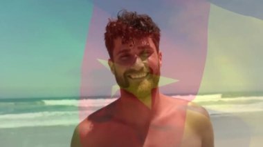 Kamerun bayrağının güneşli sahilde gülümseyen beyaz adamın üzerindeki görüntüsü. Yaz, tatiller, refah, vatanseverlik ve seyahat, dijital olarak üretilen video..