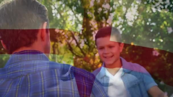 在阳光灿烂的花园里 在快乐的高加索父亲和儿子的怀抱中 升起了英国国旗的动画 英格兰 度假和爱国主义 数码视频 — 图库视频影像