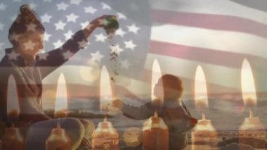Amerikan bayrağı animasyonu ve kumsalda oynayan beyaz anne ve çocuğun üzerindeki mumlar. Amerika, annelik, çocukluk, tatiller, kutlama ve vatanseverlik, dijital olarak üretilen video.