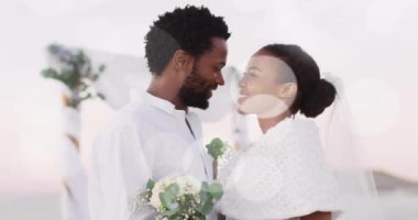 Düğünde kumsalda kucaklaşan mutlu Afrikalı Amerikalı gelin ve damadın üzerindeki ışık noktalarının animasyonu. Romantizm, aşk, tatiller ve evlilik, dijital olarak üretilen video.