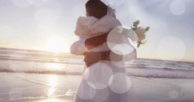 Düğünde kumsalda kucaklaşan mutlu Afrikalı Amerikalı gelin ve damadın üzerindeki ışık noktalarının animasyonu. Romantizm, aşk, tatiller ve evlilik, dijital olarak üretilen video.