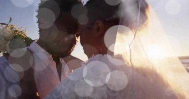 Düğünde kumsalda kucaklaşan mutlu Afrikalı Amerikalı gelin ve damadın üzerindeki ışık noktalarının animasyonu. Romantizm, aşk, tatiller ve evlilik, dijital olarak üretilen video.
