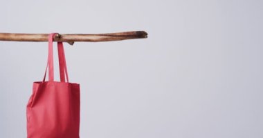Kırmızı bir çanta tahta bir çubuğa asılı, düz bir zemine, fotokopi alanı ile. Basitliği sürdürülebilir ve çevre dostu moda veya alışveriş uygulamalarına odaklanmayı öneriyor.