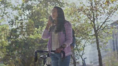 Şehir parkında bisikletli bir kadının telefonda konuştuğu grafik üzerindeki veri işleme animasyonu. Ağ, veri, iş hayatı, şehir hayatı, dijital arayüz ve iletişim, dijital olarak oluşturulmuş video.