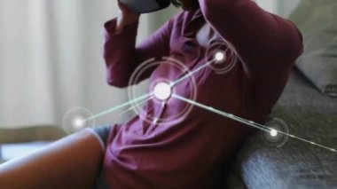 Evde video kulaklığı kullanan beyaz bir kadın üzerinden iletişim ağının animasyonu. Ağ, dijital arayüz, ev hayatı, yaşam tarzı ve iletişim, dijital olarak oluşturulmuş video.