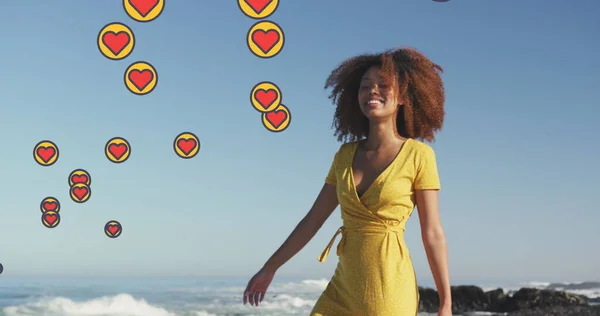 Image of heart digital icons over woman dancing on beach. digital interface, social media and global technology concept digitally generated image.